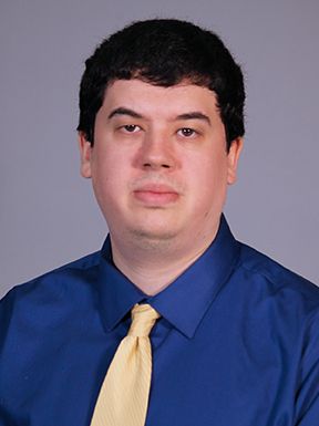 Headshot of Dr. Nathan Galinsky in a blue shirt and yellow tie against a gray background
