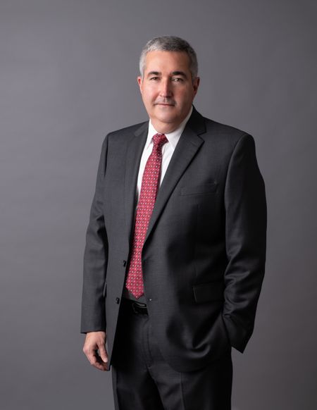 Photo of Kevin Highlander in a suit standing in front of a grey professional background